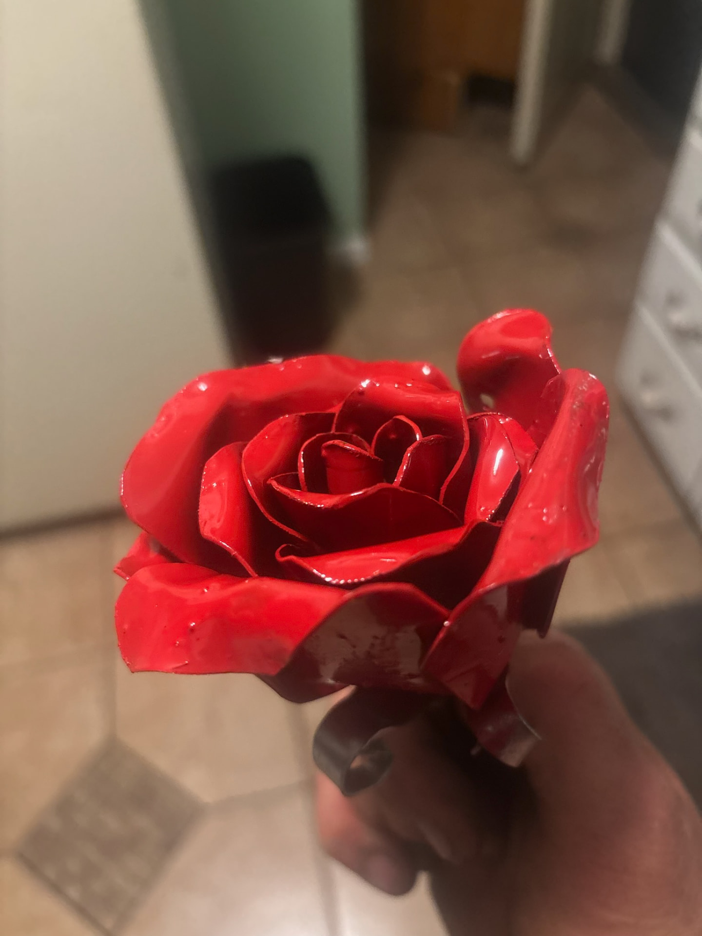 Close view of a forged steel rose finished in glossy red enamel, held in a hand