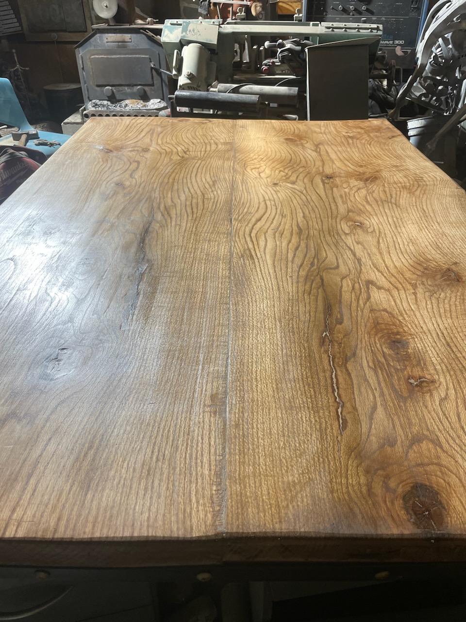 Live-edge white oak slab table top with visible grain and knots, sitting on a steel base in the workshop