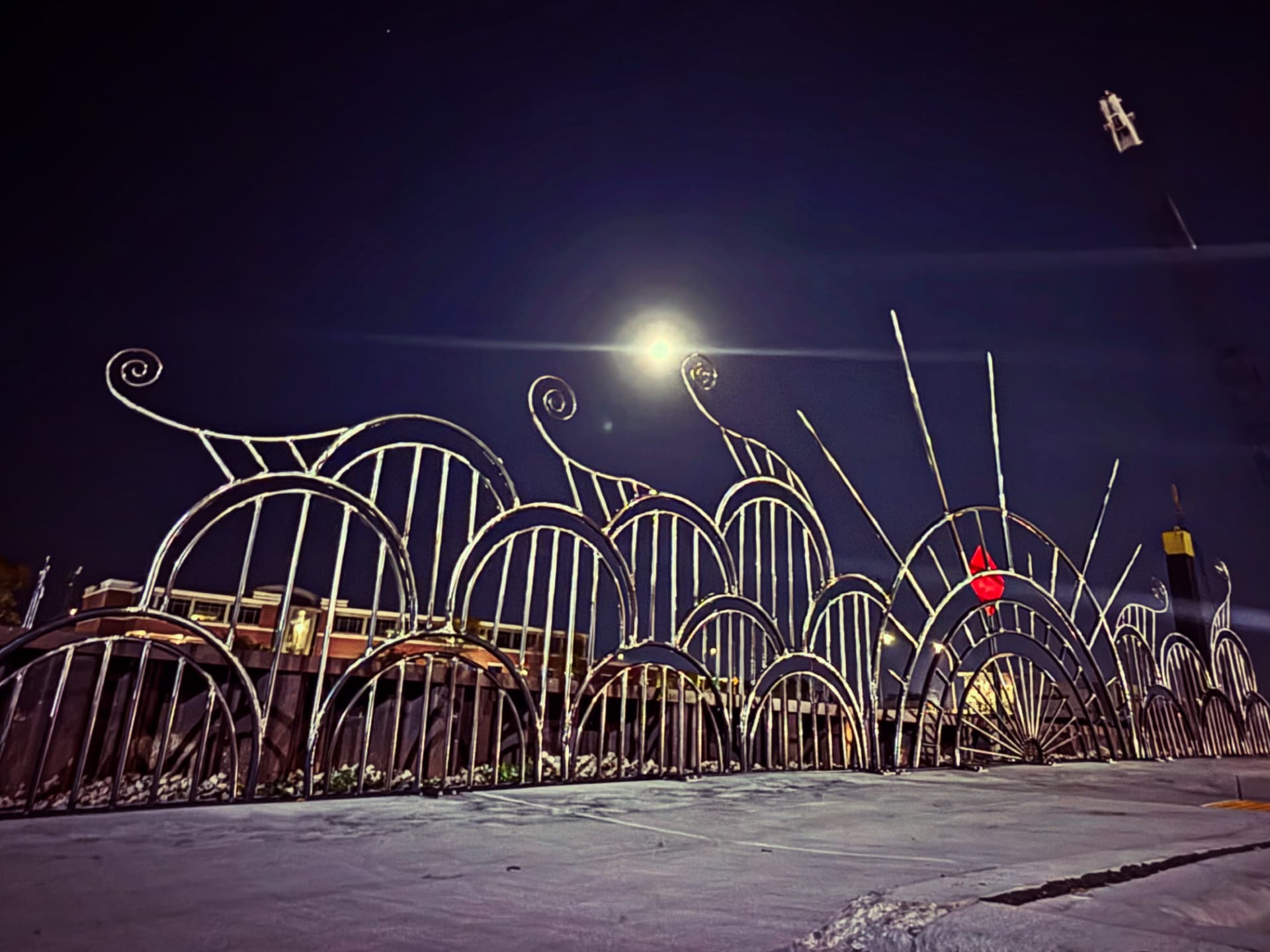 Arched polished steel railing sculpture along the Manitowoc riverfront at night, lit under a full moon, reflecting light like waves on water